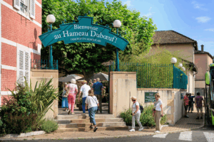 Bienvenue au Hameau Dubœuf. Les visiteurs franchissent l'entrée principale du parc à Romanèche-Thorins, où commence leur découverte des espaces de visite, des animations et des expériences consacrés à la vigne, au vin et au Beaujolais.